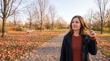 Frau mit braunen Haaren im herbstlichen Park mit Laub auf dem Weg – saisonaler Haarausfall im Herbst